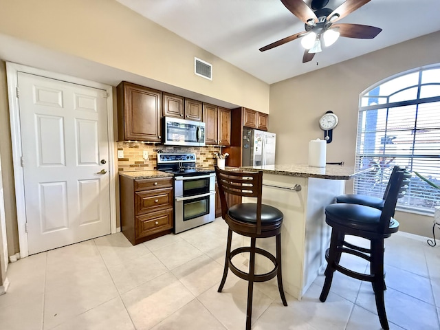 kitchen with a kitchen breakfast bar, backsplash, light stone countertops, and stainless steel appliances