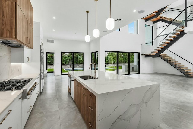 kitchen featuring light stone countertops, sink, pendant lighting, white cabinetry, and an island with sink