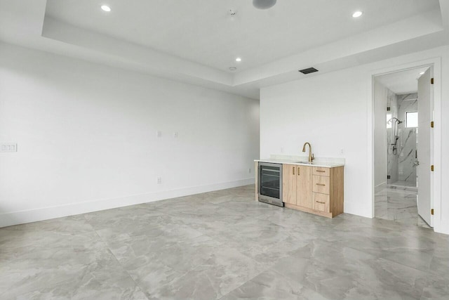 bar with a raised ceiling, wine cooler, light brown cabinets, and sink