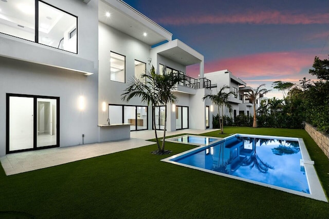 back house at dusk featuring a patio area, a balcony, and a yard