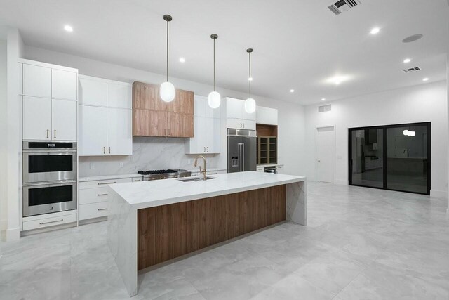 kitchen featuring white cabinetry, sink, an island with sink, decorative light fixtures, and appliances with stainless steel finishes