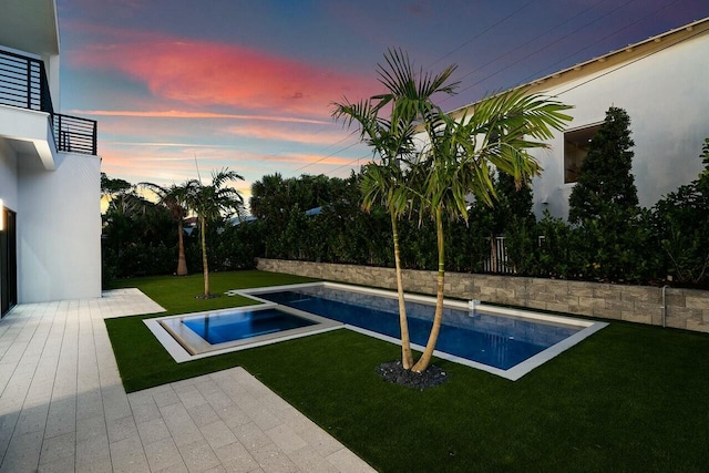 pool at dusk featuring a lawn and an in ground hot tub