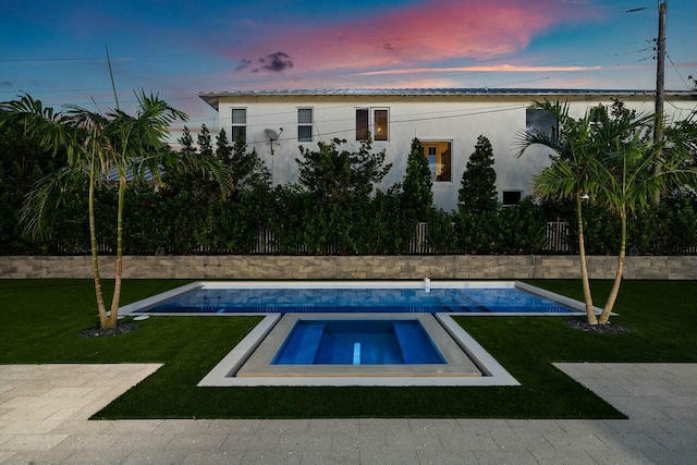 pool at dusk with a lawn and an in ground hot tub