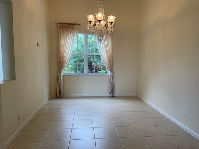 tiled spare room featuring a notable chandelier