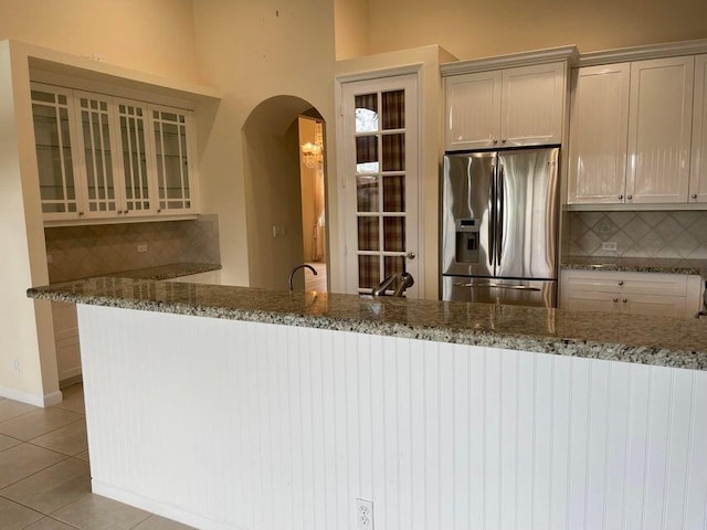 kitchen with backsplash, kitchen peninsula, stone countertops, light tile patterned flooring, and stainless steel fridge with ice dispenser