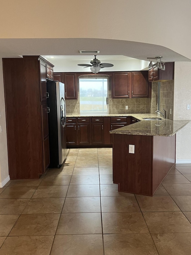 kitchen with kitchen peninsula, light stone countertops, backsplash, sink, and stainless steel fridge with ice dispenser