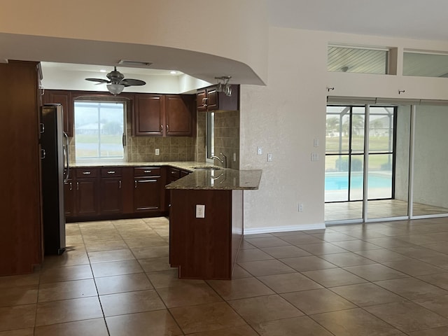 kitchen featuring stone counters, sink, ceiling fan, stainless steel fridge, and kitchen peninsula