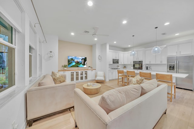 living room featuring ceiling fan, sink, and light wood-type flooring