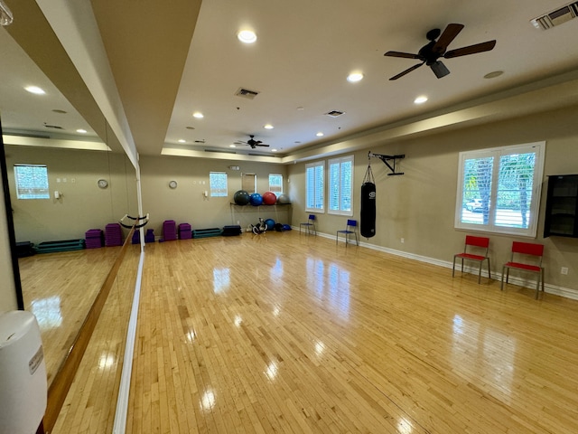 workout room with a tray ceiling, ceiling fan, and light hardwood / wood-style flooring