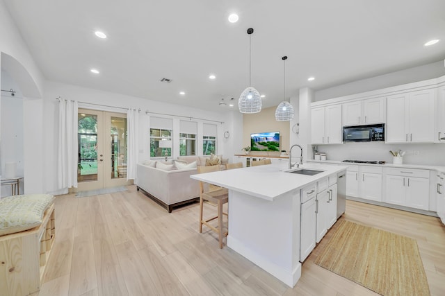 kitchen with french doors, a center island with sink, white cabinets, sink, and decorative light fixtures