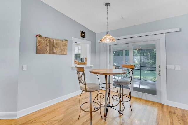 dining space with a healthy amount of sunlight, light wood-type flooring, and vaulted ceiling