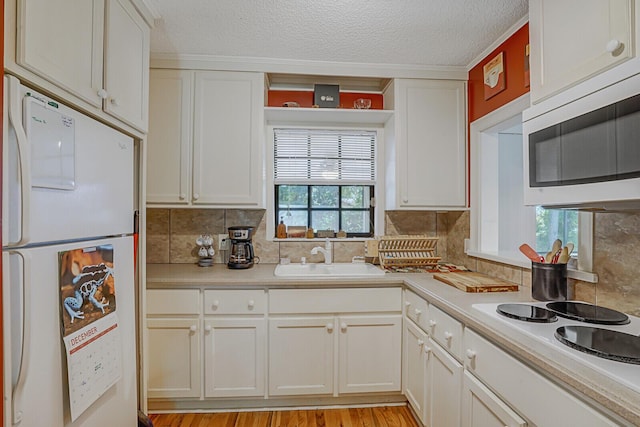 kitchen with light wood-type flooring, a textured ceiling, white appliances, sink, and white cabinetry