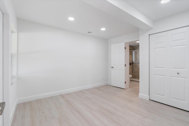 unfurnished bedroom with ensuite bathroom, a closet, and light hardwood / wood-style floors