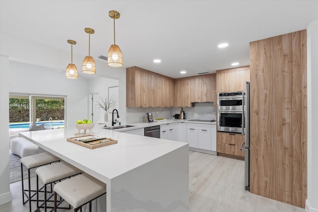 kitchen with a kitchen breakfast bar, stainless steel appliances, sink, pendant lighting, and white cabinets