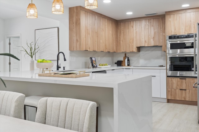 kitchen with tasteful backsplash, double oven, pendant lighting, white cabinets, and light wood-type flooring