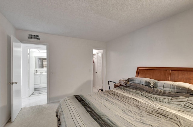 carpeted bedroom featuring a closet, a textured ceiling, and ensuite bath