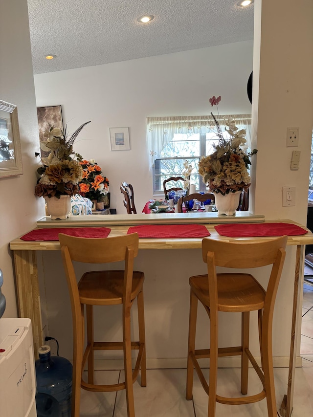 kitchen featuring a kitchen bar, a textured ceiling, kitchen peninsula, and light tile patterned flooring