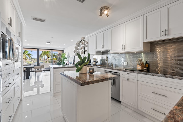 kitchen featuring white cabinets, stainless steel dishwasher, a kitchen island, and dark stone countertops