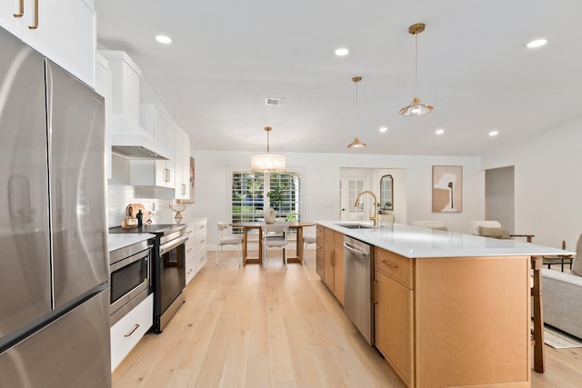 kitchen with appliances with stainless steel finishes, decorative light fixtures, white cabinetry, sink, and a large island with sink