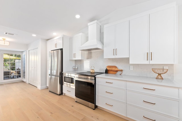 kitchen with appliances with stainless steel finishes, backsplash, white cabinets, light hardwood / wood-style floors, and custom range hood