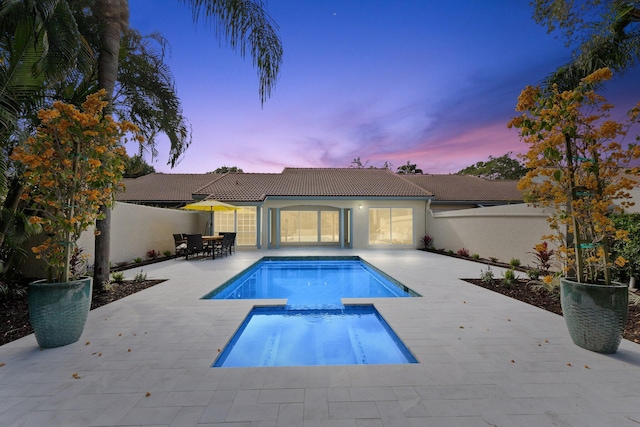 pool at dusk with an in ground hot tub and a patio area