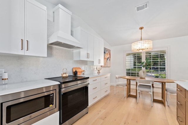 kitchen with premium range hood, white cabinetry, hanging light fixtures, stainless steel microwave, and stove