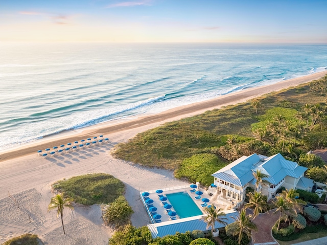 aerial view at dusk featuring a water view and a view of the beach