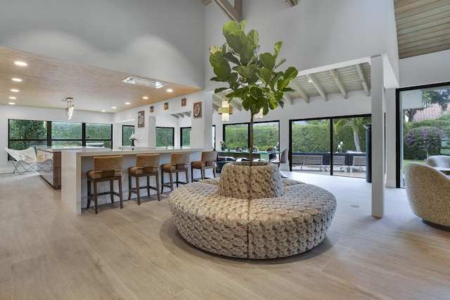 living room featuring beamed ceiling, a towering ceiling, wooden ceiling, and light wood-type flooring