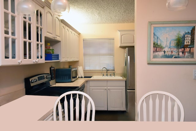 kitchen with stove, a textured ceiling, white cabinetry, and sink