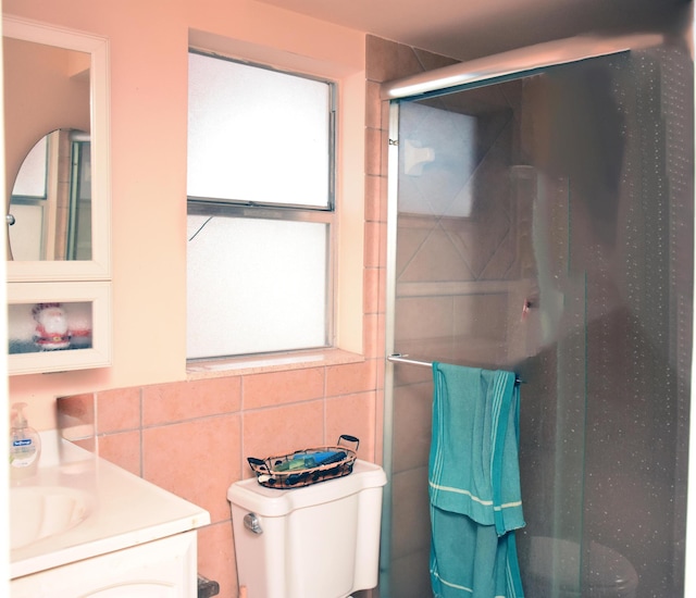 bathroom featuring vanity, toilet, tile walls, and a shower with shower door