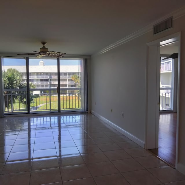 empty room featuring tile patterned floors, visible vents, floor to ceiling windows, crown molding, and baseboards