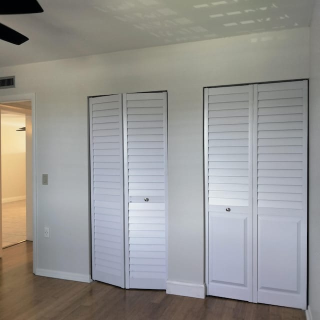 unfurnished bedroom with visible vents, baseboards, dark wood-style floors, and multiple closets