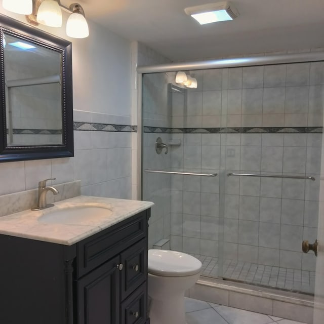 bathroom with toilet, a stall shower, tile walls, tile patterned flooring, and vanity