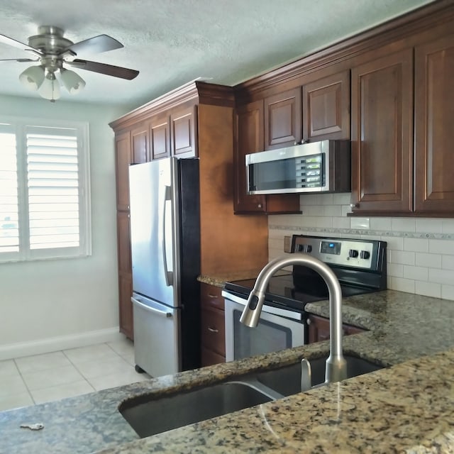 kitchen featuring a ceiling fan, tasteful backsplash, stainless steel appliances, light tile patterned flooring, and light stone countertops