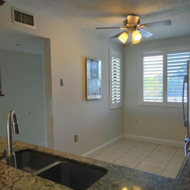 kitchen featuring visible vents, a sink, light stone counters, light tile patterned floors, and ceiling fan