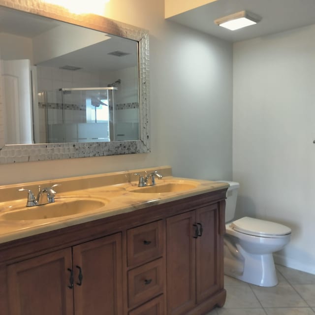 bathroom with double vanity, a stall shower, a sink, tile patterned flooring, and toilet