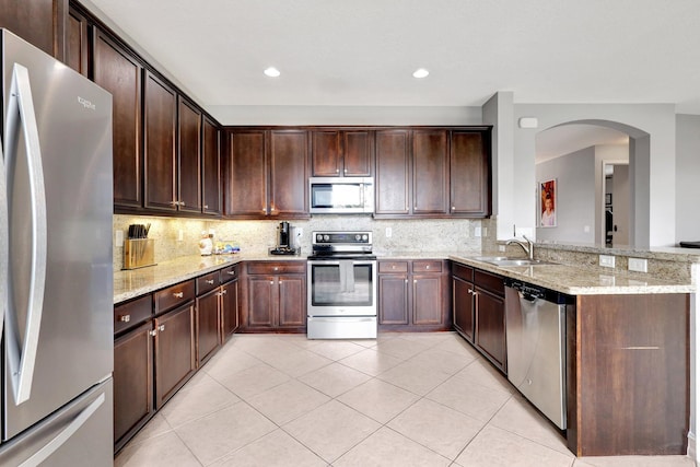 kitchen featuring appliances with stainless steel finishes, light stone counters, dark brown cabinetry, tasteful backsplash, and light tile patterned flooring