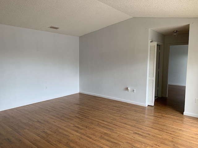 spare room with lofted ceiling, wood-type flooring, and a textured ceiling