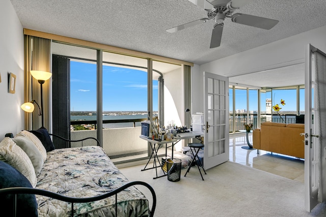 bedroom with french doors, floor to ceiling windows, a textured ceiling, ceiling fan, and a water view