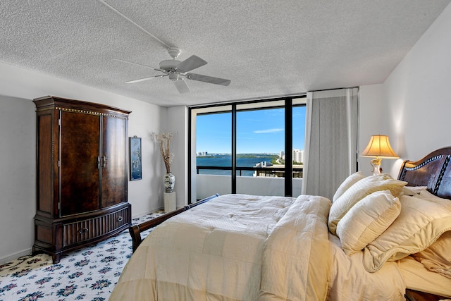 carpeted bedroom with access to exterior, ceiling fan, a water view, and a textured ceiling