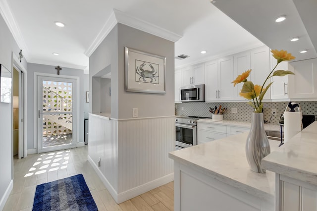 kitchen with stainless steel appliances, light stone counters, decorative backsplash, white cabinets, and ornamental molding