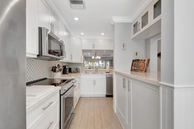 kitchen featuring light stone countertops, stainless steel appliances, crown molding, sink, and white cabinets