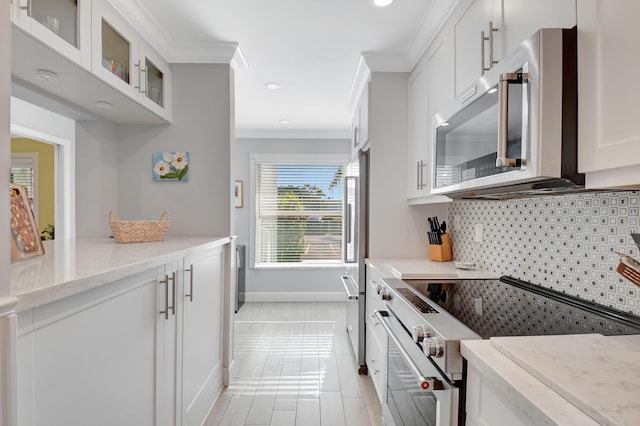 kitchen featuring white cabinetry, ornamental molding, light stone counters, and appliances with stainless steel finishes