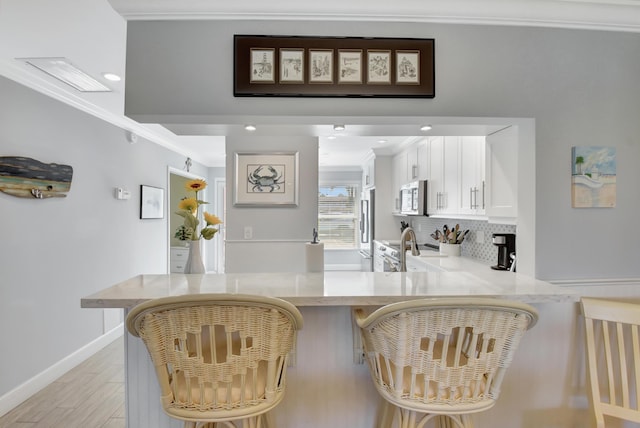 bar with white cabinets, light hardwood / wood-style flooring, decorative backsplash, ornamental molding, and appliances with stainless steel finishes