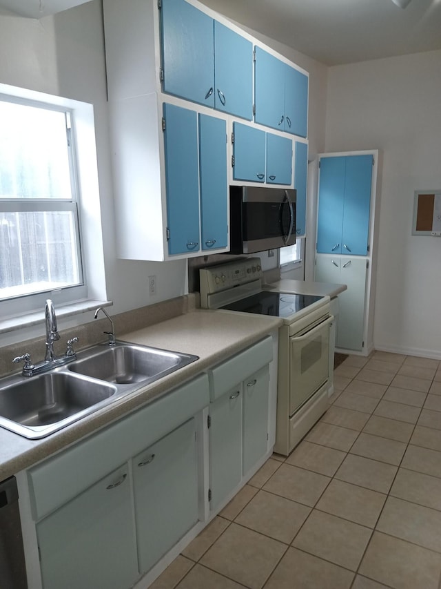 kitchen with white cabinets, blue cabinets, sink, light tile patterned floors, and appliances with stainless steel finishes