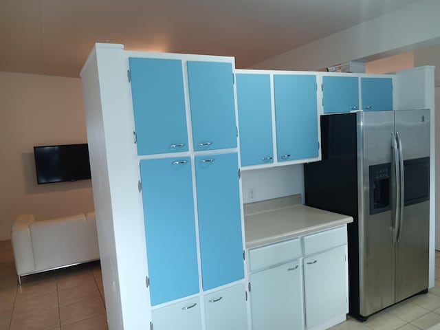 kitchen featuring white cabinets, stainless steel refrigerator with ice dispenser, light tile patterned floors, and blue cabinetry