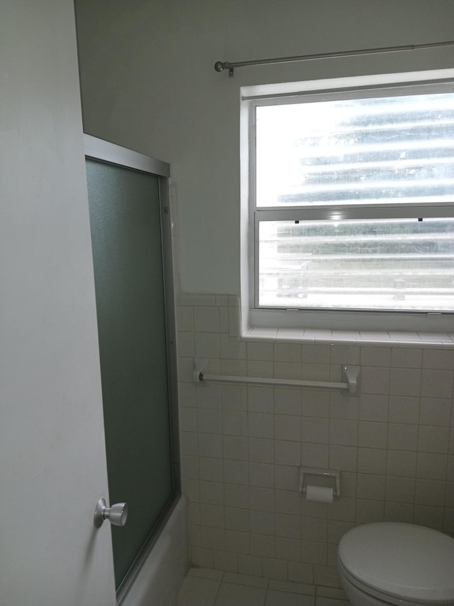 bathroom featuring tile patterned flooring, toilet, and enclosed tub / shower combo