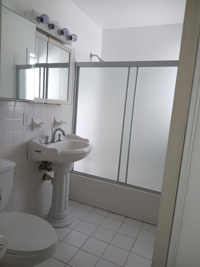 bathroom featuring shower / bath combination with glass door, backsplash, tile patterned flooring, toilet, and tile walls