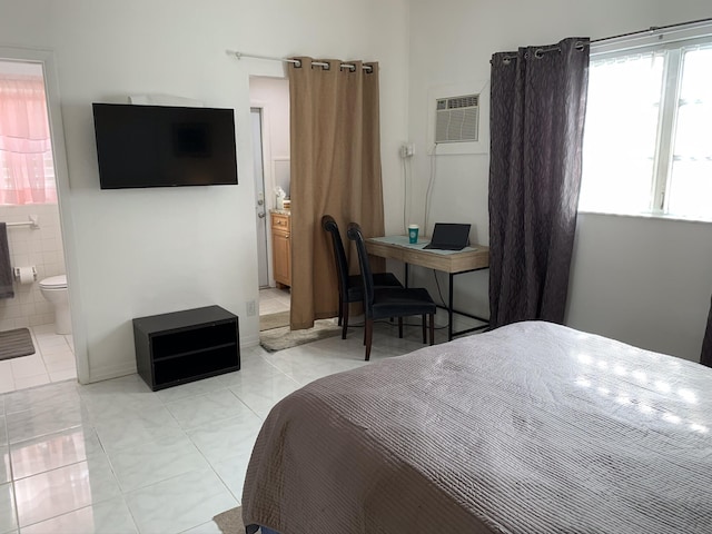 bedroom with a wall unit AC, light tile patterned floors, and connected bathroom