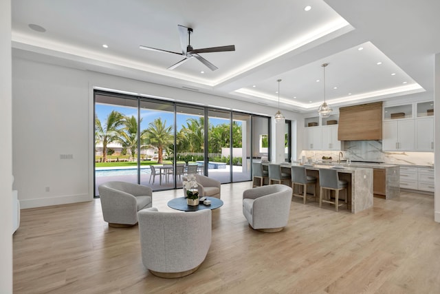 living room featuring ceiling fan, sink, light hardwood / wood-style flooring, and a tray ceiling